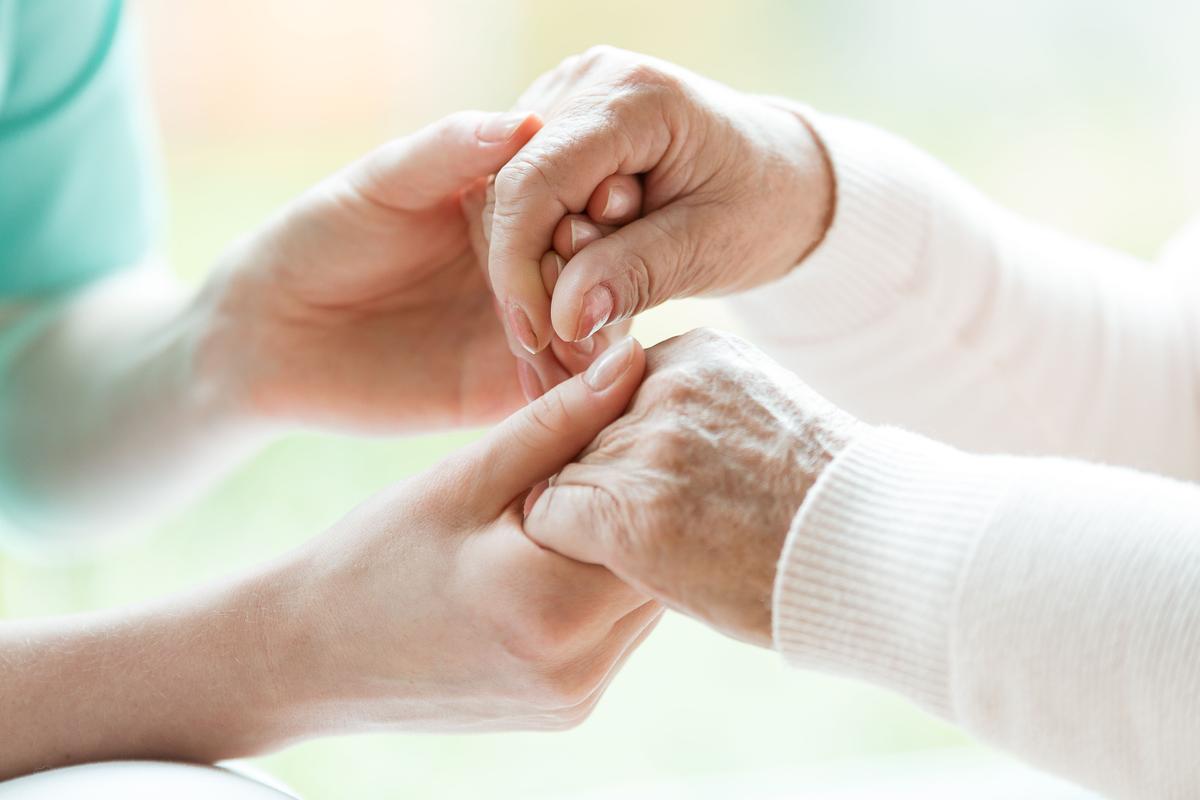 Verpleegkundige houdt handen van oudere vrouw vast